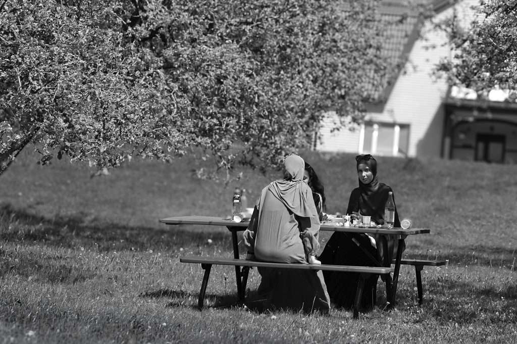 Kvinnor sitter vid ett picknickbord under träd i en park, svartvit gatufoto