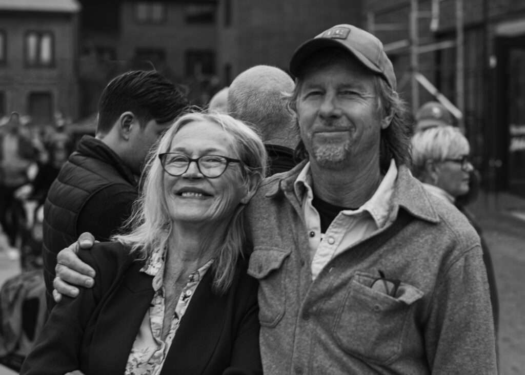 Anne och Daniel står tätt ihop och ler, han med armen om hennes axel, mitt i folksamlingen vid gamla slakteriområdet.