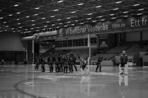Frillesås BK samlade i en ring på isen före bandymatchen mot VSK i ABB Arena Syd, med målvakten till höger och tomma läktare bakom.